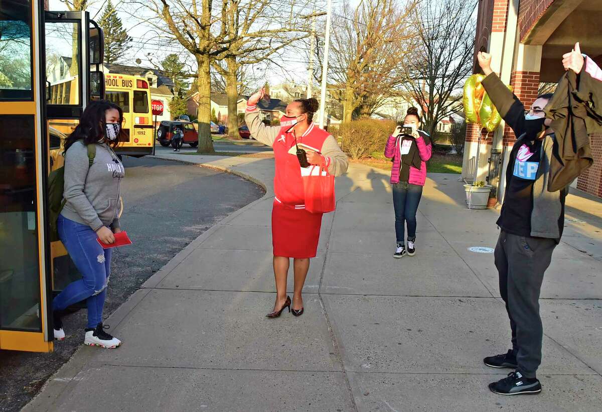 New Haven, Connecticut: Monday - April 5, 2021: Wilbur Cross H.S. principal Edith Johnson, second from left, and school psychologist Michael Awad, far right, greet students at the front of the school as all New Haven High Schools reopen Monday morning with the easing of Covid-19 pandemic restrictions.
