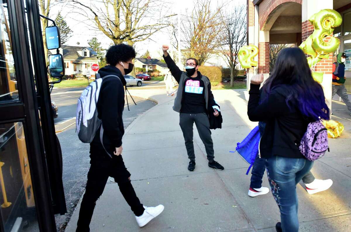 New Haven, Connecticut: Monday - April 5, 2021: Wilbur Cross H.S. school psychologist Michael Awad, center, greets students at the front of the school as all New Haven High Schools reopen Monday morning with the easing of Covid-19 pandemic restrictions.
