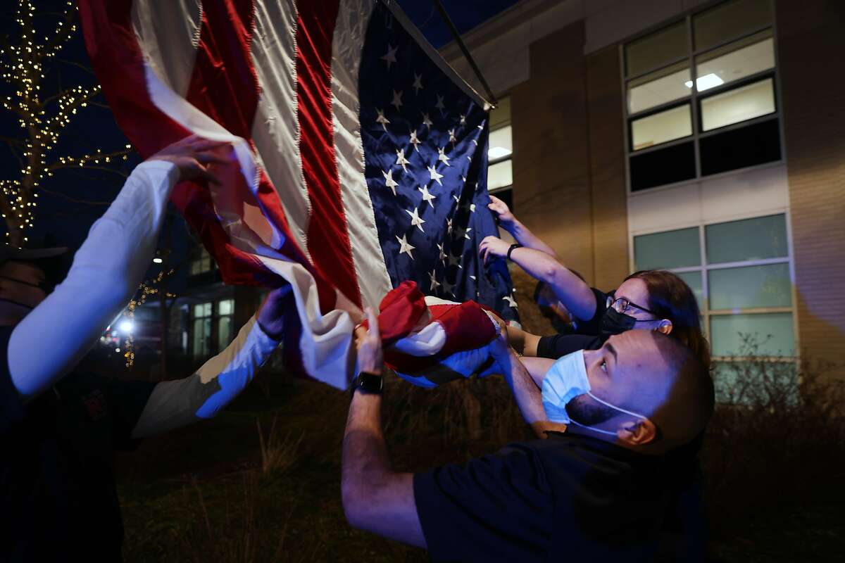 An American flag is raised as firefighters, medical workers, first responders and members of the public gather in front of a hospital in Mount Kisco, N.Y., on March 11, 2021, to mark the one-year anniversary of the first Covid-19 patient admission there.