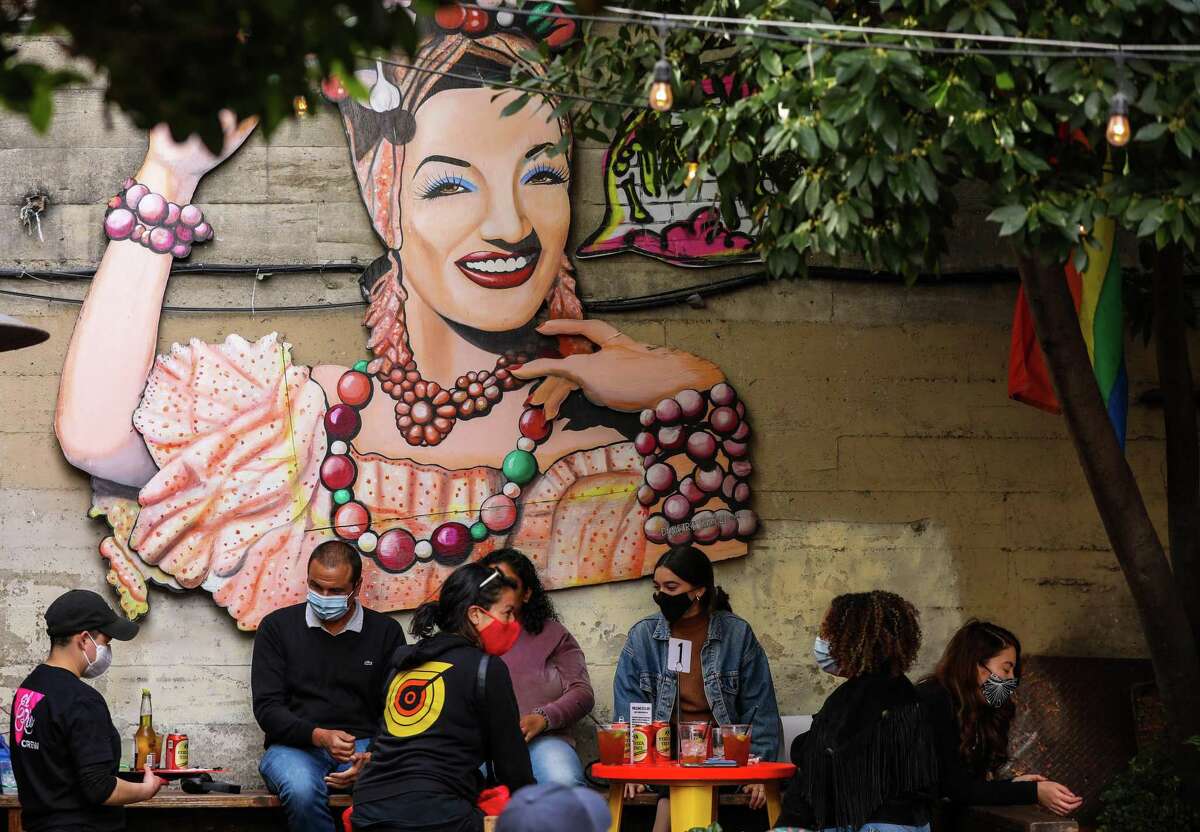 Patrons enjoy drinks on the patio of El Rio in front of a mural of samba singer Carmen Miranda.