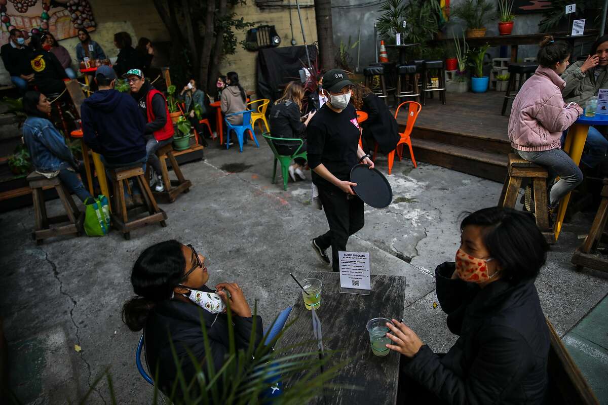 Shivani Rangwala, bottom left (donning avocado mask), and her friend Elin Chee, bottom right (donning fig mask), listen to manager Cynthia Martinez as she converses with them during their visit to El Rio, located at 3158 Mission St., on Saturday, April 3, 2021, in San Francisco, Calif. California will retire its color-coded pandemic blueprint on June 15 and allow almost all sectors of the economy, in all 58 counties, to reopen at or near full capacity, state officials said Tuesday.