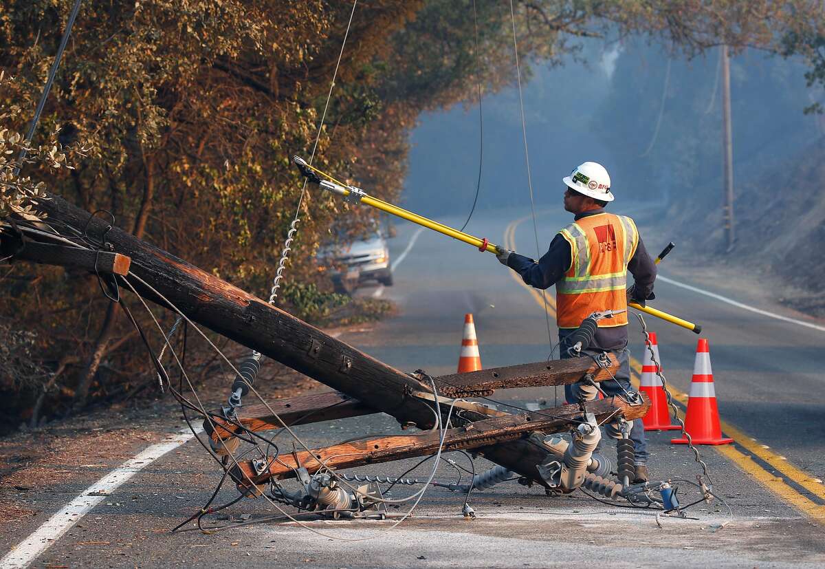 A PG&E worker severs the power line from a fallen utility pole on Geysers Road as the Kincade Fire burns near Geyserville in October 2019.