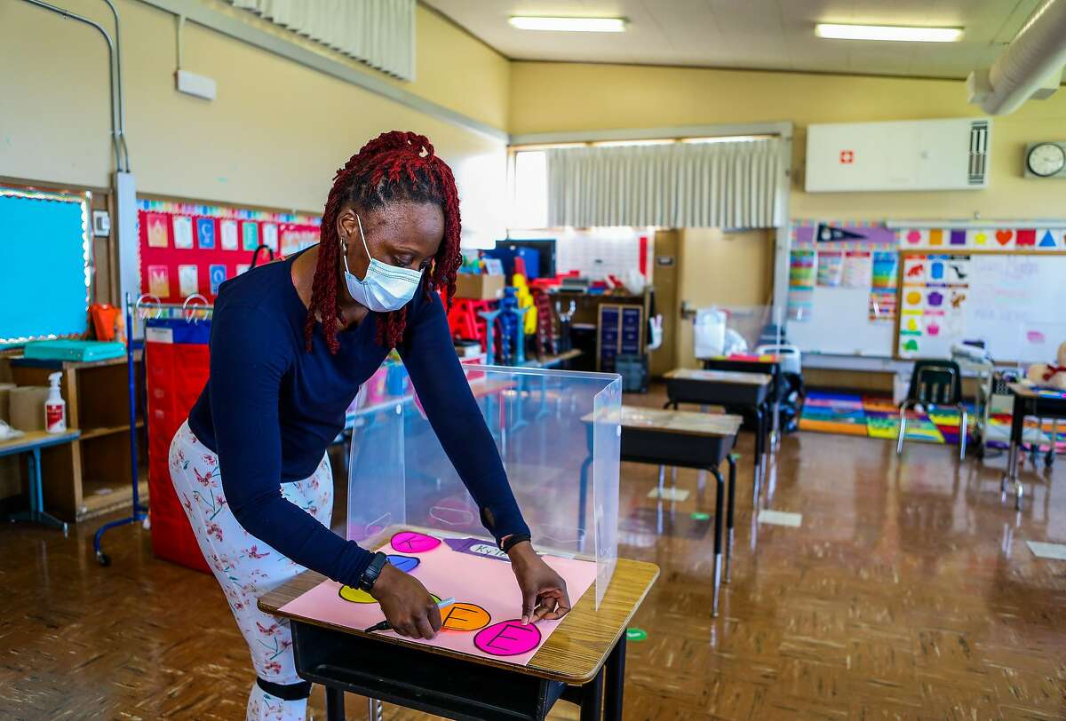 Shaione Simmons, who teaches transitional kindergarten and kindergarten, places a student's name on a desk as she preps her classroom at Madison Park Academy Primary on Thursday, March 25, 2021, in Oakland, Calif. The school is preparing to reopen on Tuesday.