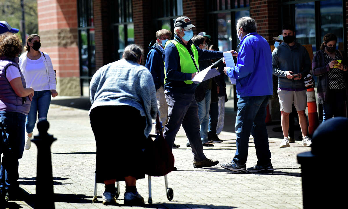 Volunteers help local residents line up at the Ultimate Regent 8 movie theater where the Norwalk Health Department held a mass COVID vaccination clinic in the lobby of the theater Wednesday, April 7, 2021, in Norwalk, Conn. The Bow Tie Cinemas theater owner partnered with the healtth department to host the public COVID vaccination clinic.