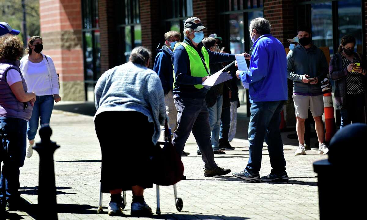 Volunteers help local residents line up at the Ultimate Regent 8 movie theater where the Norwalk Health Department held a mass COVID vaccination clinic in the lobby of the theater Wednesday, April 7, 2021, in Norwalk, Conn. The Bow Tie Cinemas theater owner partnered with the healtth department to host the public COVID vaccination clinic.
