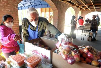 Volunteer Tony Montemurno, of Stratford, reaches for a bag of apples as he assists a woman picking up groceries at the weekly food pantry event outside Bridgeport Rescue Mission's new Community Care Clinic, currently under construction in Bridgeport, Conn. April 8, 2021.