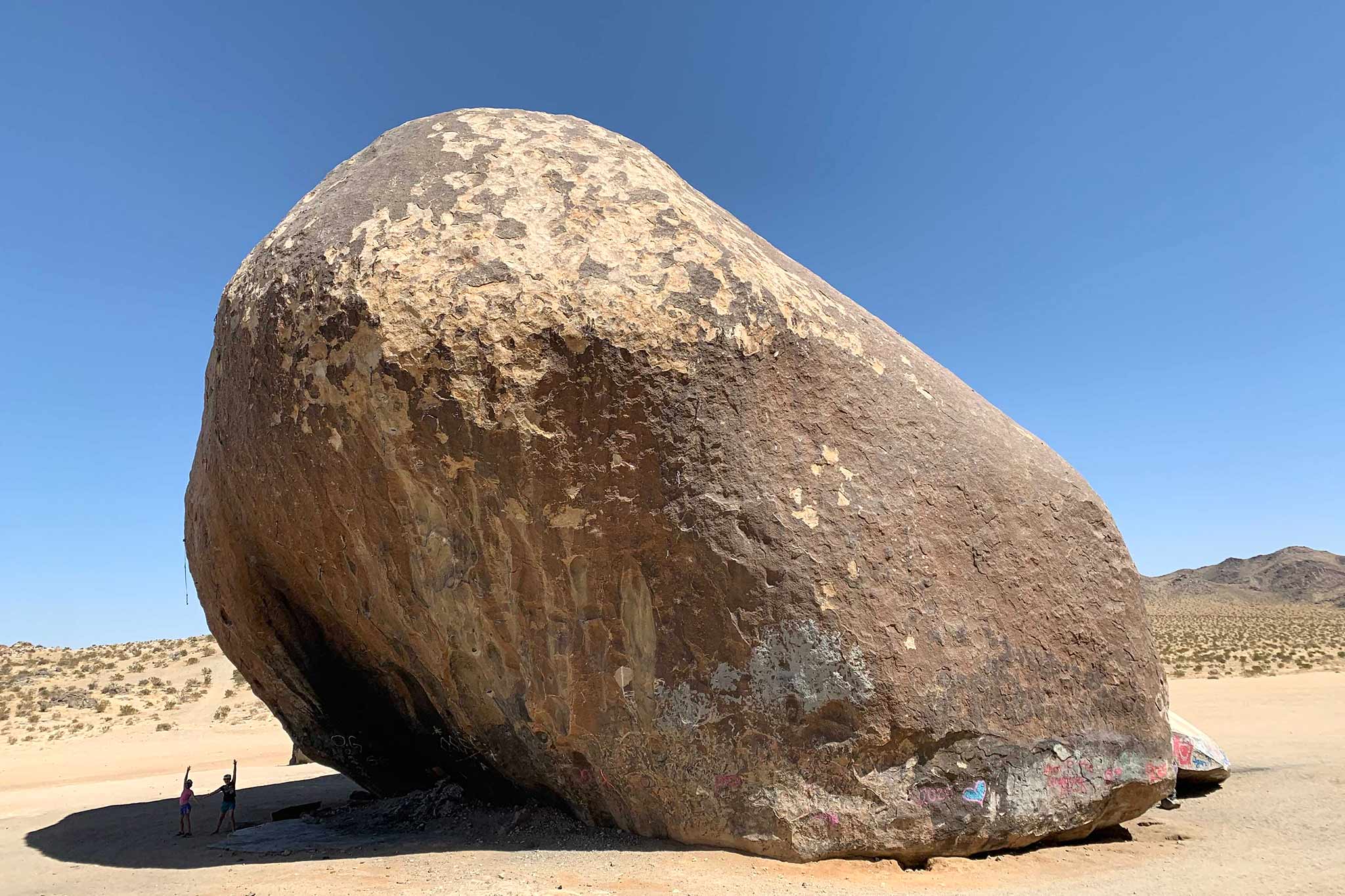 Large boulder in desert sands with clear blue skies and sandy brush in the background