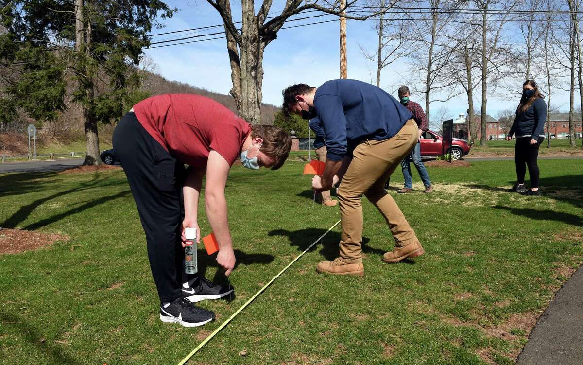 Quinnipiac University juniors Kyle Somogyi, left, and Mike Neumann of the student chapter of the American Society of Civil Engineers plant flags to mark a rough outline where society members are building a rain garden to protect runoff from the Albert Schweitzer Institute seeping into the Mill River, on April 9, 2021.