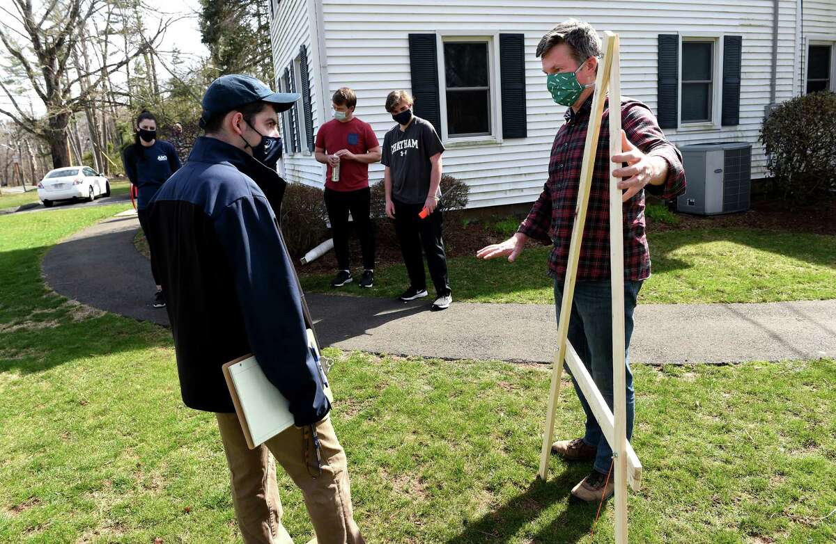Sean Duffy, right, executive director of the Albert Schweitzer Institute, demonstrates a rudimentary level for mapping contours of the land to Michael Ciacciarella, president of the Quinnipiac University student chapter of the American Society of Civil Engineers, on April 9, 2021, where society members are building a rain garden to protect runoff from the Albert Schweitzer Institute seeping into the Mill River.