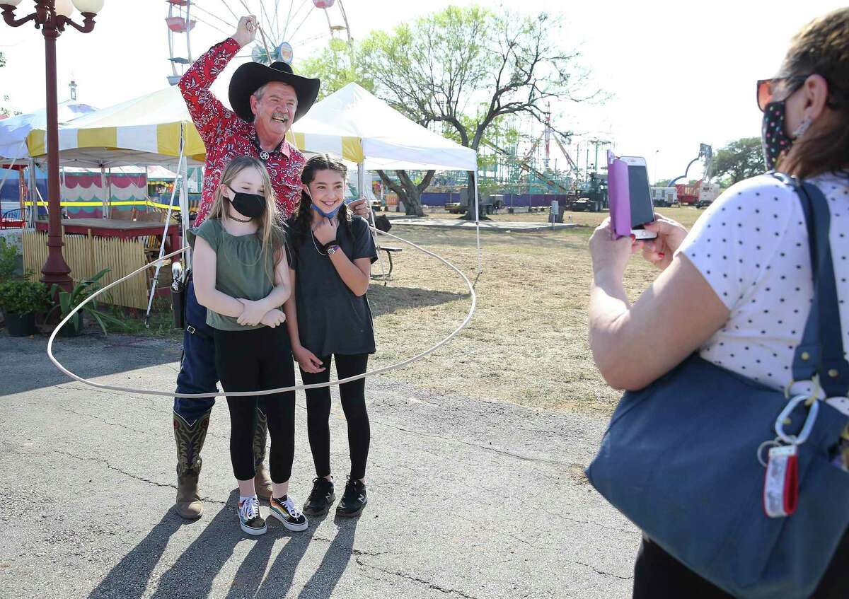 Cowboy Doug Whitaker performs a lasso trick around friends Alyssa Marquez, right, and Allison King as Marquez's mother, Beverly, snaps a picture Friday. The Poteet Strawberry Festival kicked off Thursday evening. It was canceled last year.