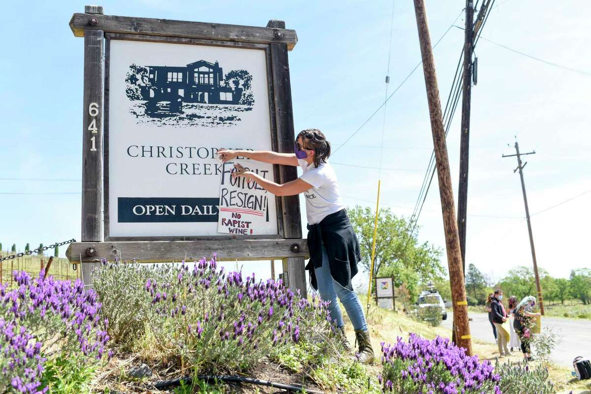 Hollie Clausen of Santa Rosa puts a sign calling for Windsor Mayor Dominic Foppoli to resign on the sign for Christopher Creek Winery at a rally in Healdsburg.