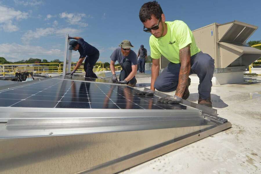 ENCON employees including C.J. Pappas, left, install solar panels on the roof of the Paul Miller Nissan dealership in Fairfield on July 18, 2018. The project received financing from Darien-based Greenworks Lending, which has been acquired by global investment manager Nuveen.