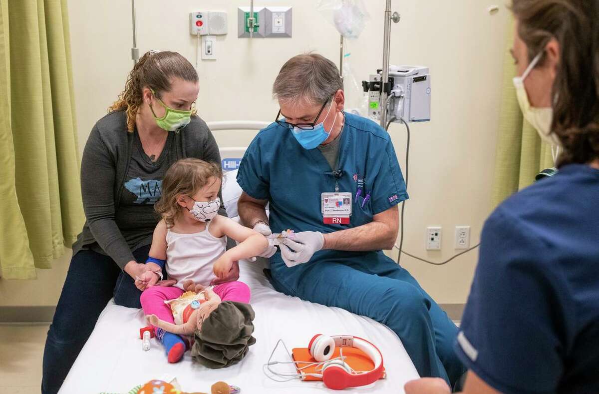 Angelica LaCour, left, sits with her daughter Eloise LaCour, 3, as she gets vaccinated by registered nurse Rich Brotherton while a colleague looks on at Clinical and Translational Research Unit at Stanford Medicine in Stanford on April 14. Eloise was among the first to get a shot in a Pfizer trial of young children at Stanford.