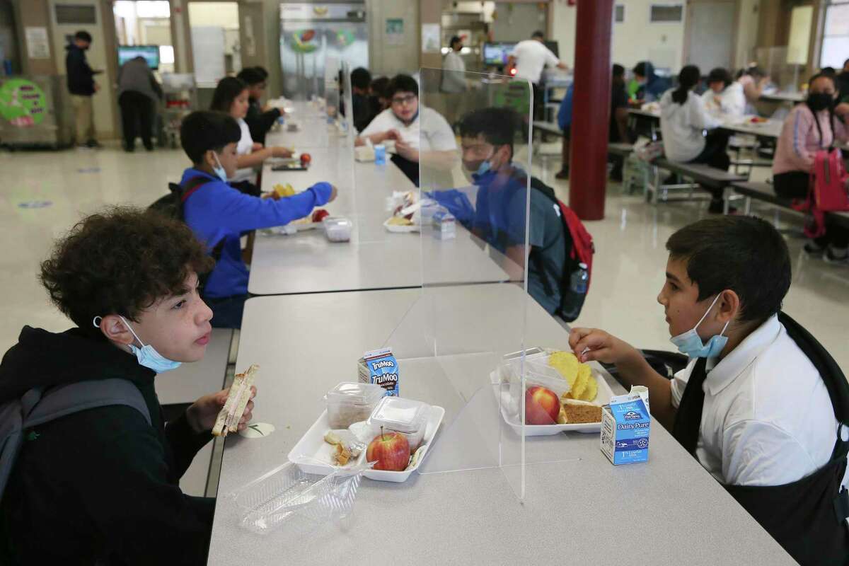 Students sit in pairs separated by plexiglass while eating lunch at Rhodes Middle School this spring. Several San Antonio school districts will offer free meals to all students during the upcoming school year.