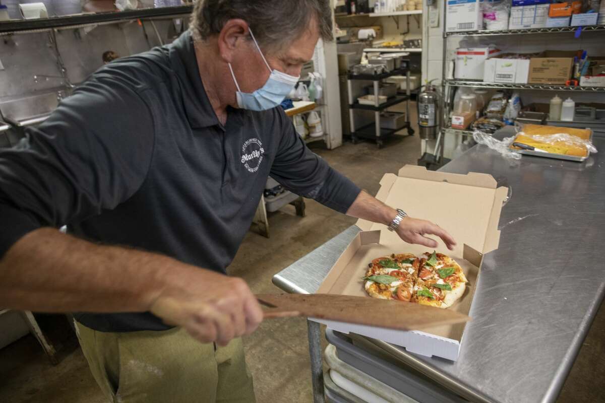 Murray’s Deli added wood fired brick oven pizza to the menu in February. Scott Dufford slides a Dufford Classic pizza in a take-out box.