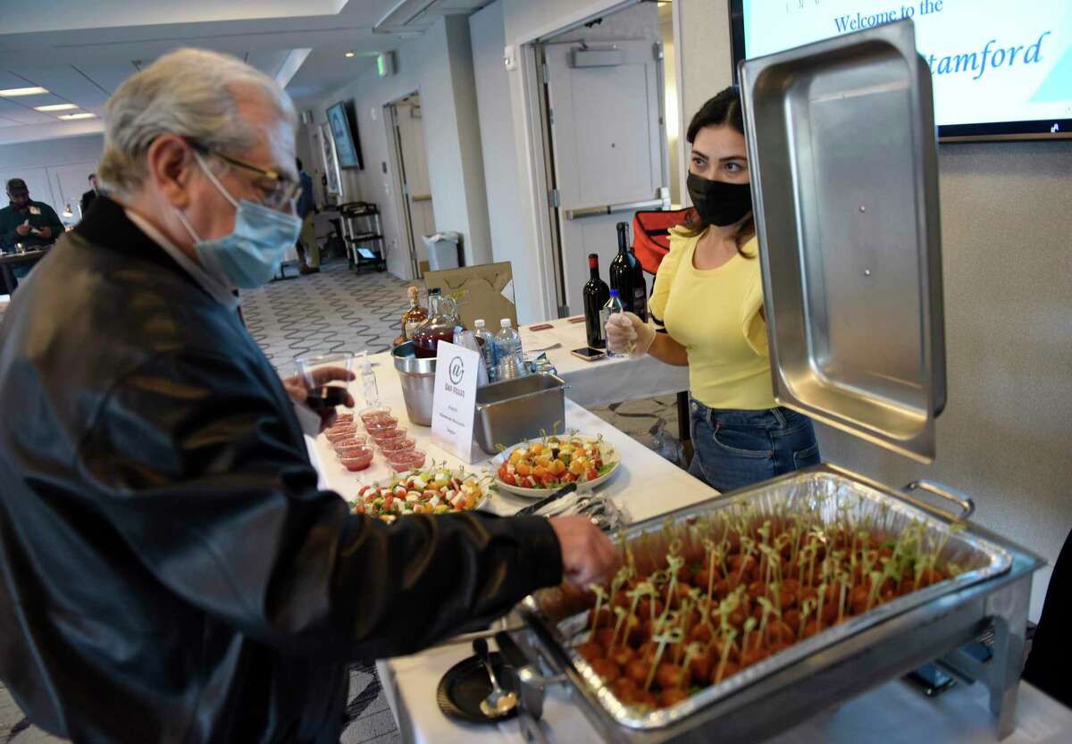 David Goldvug samples arancini from Erika Mikoshi at Bar Rosso's booth at the "Mini Taste of Stamford" event at Residence Inn by Marriott in Stamford, Conn. Wednesday, April 14, 2021. Presented by Stamford Chamber of Commerce, the event featured food and drink samples from local restaurants in the hotel ballroom and outdoor terrace.