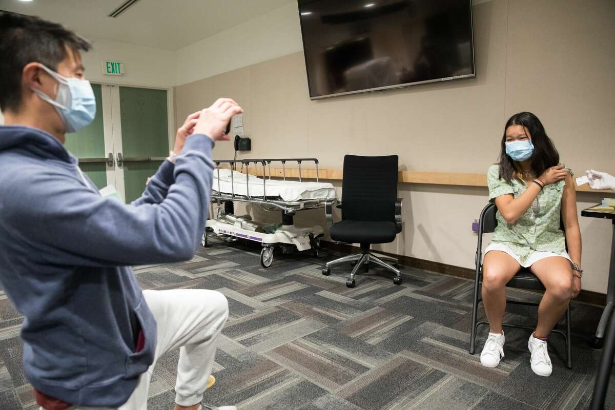 Emma Yin, 16, has her photo taken by her father Clifford Yin as she receives a COVID-19 vaccine at UCSF Benioff Children Hospital from nurse Melani Wells in Oakland, Calif. on April 15, 2021.