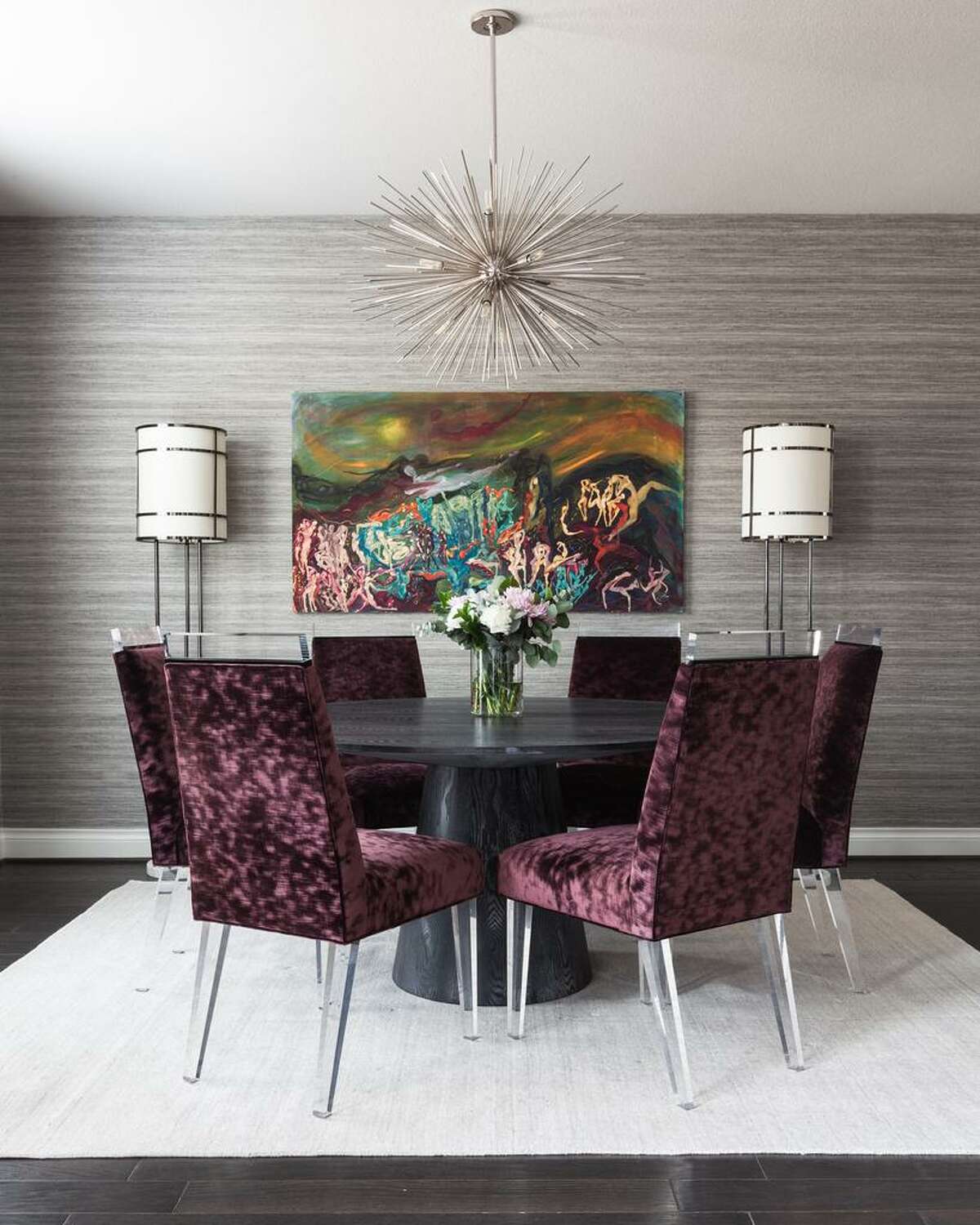 The showstopper dining room has faux grasscloth vinyl wallpaper, a chrome starburst chandelier and custom dining chairs covered in purple couture velvet and finished with acrylic legs.