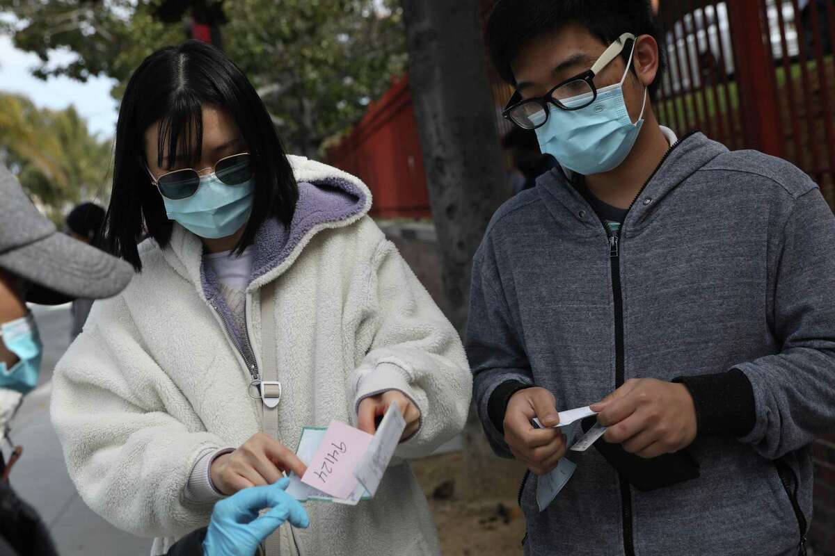 Jenny Lan (l to r) and Derren Lei show their proof of zip code and receive a number as they arrive at the end of the line at Zuckerberg General Hospital for non-appointments to recievie the COVID-19 vaccine on April 13, 2021 in San Francisco, Calif.