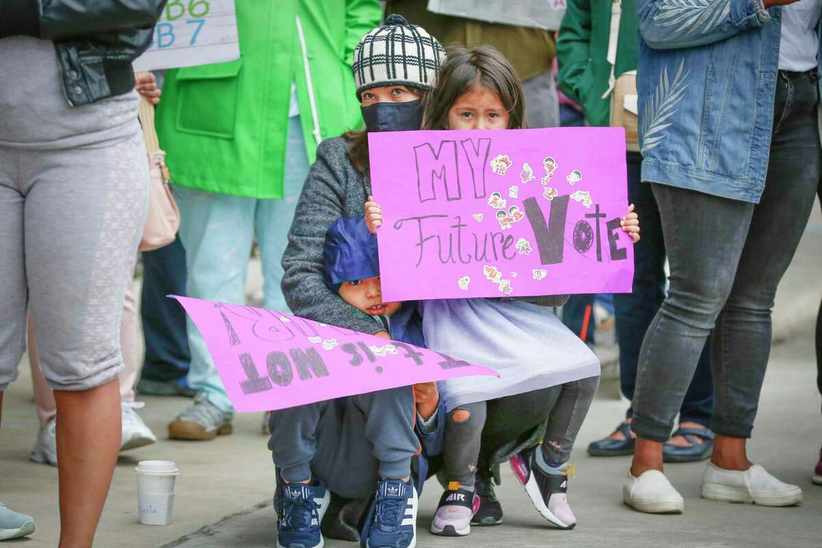 Diana Negreros (center) and her children Liam, 6 (left), and Nora, 4 (right), holds a sign with voters and activist organizations as they gather at the Greater Houston Partnership building to demand the business group oppose the voter bills being considered by the Texas legislature Saturday, April 17, 2021, in Houston.