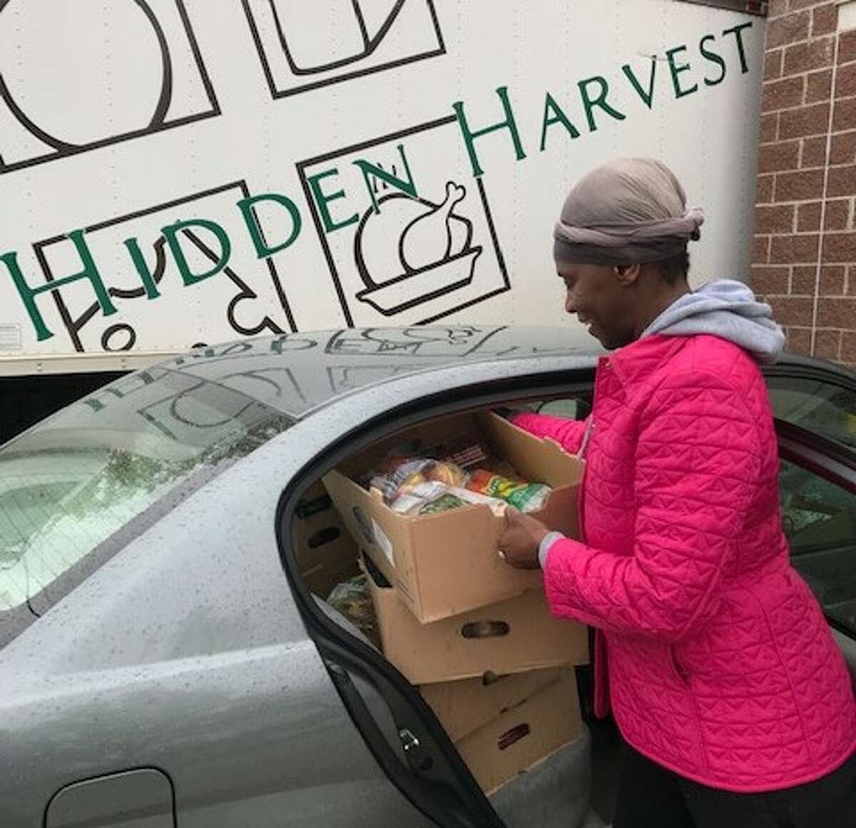 A food pantry coordinator from World Outreach Campus Church loads food donations from Hidden harvest into a car.