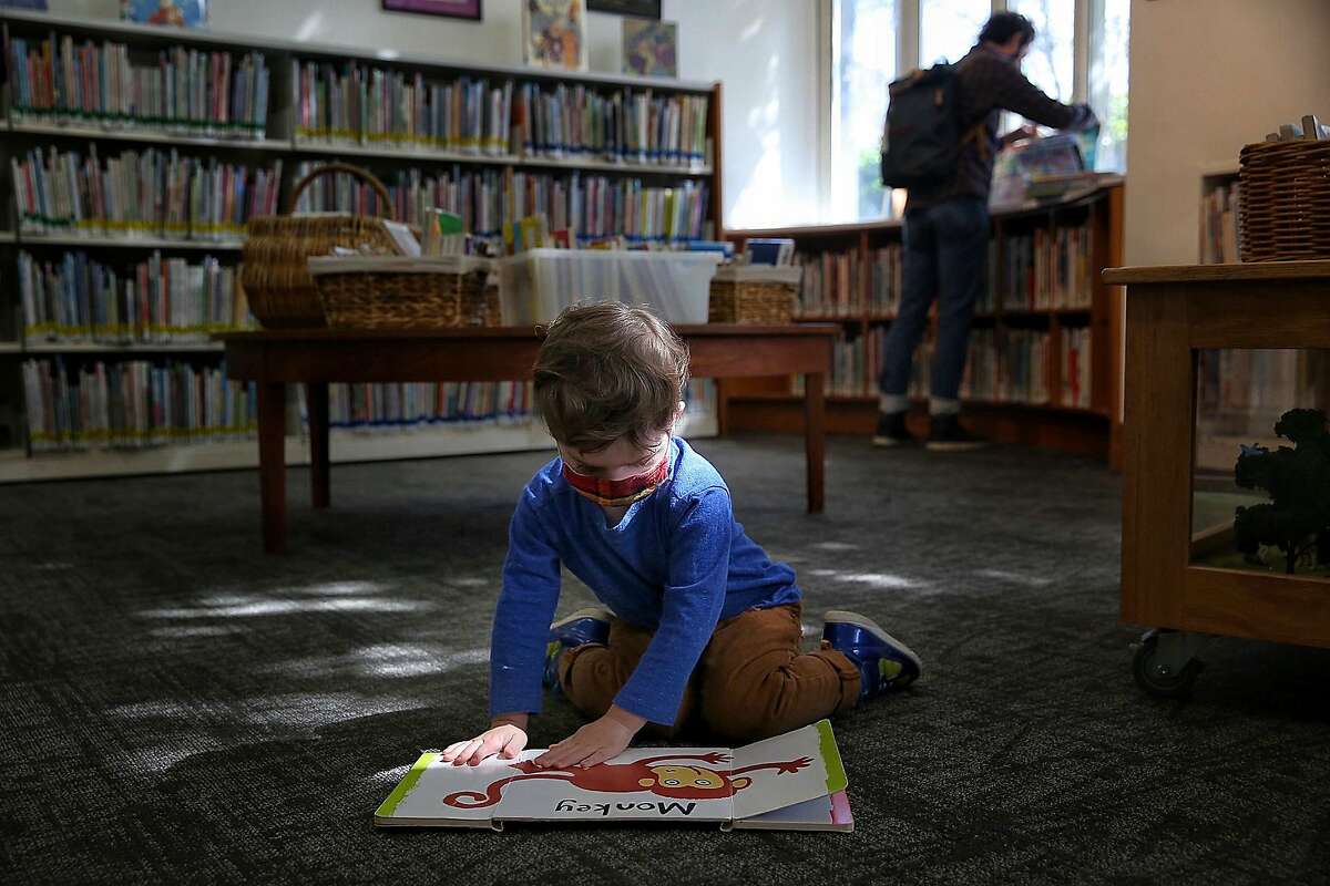 Frank, 2, opens flaps of a book as father Shawn (background) browses at the Rockridge branch of the Oakland library.