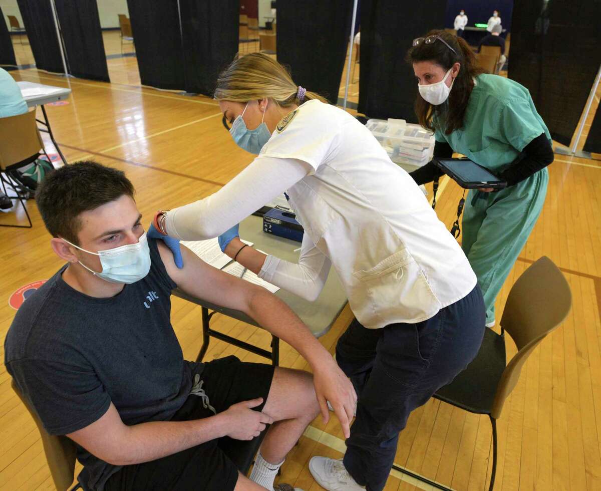 Ryan Hirt, of West Islip, NY, waits as Sophie Bjornson, of Bethel, administers a COVID-19 vaccination during a clinic at Western Connecticut State University. The clinic, held in the Bill Williams Gymnasium on the mid-town campus, was for the university's students. Tuesday, April 20, 2021, in Danbury, Conn. Hirt is a marketing major and Bjornson is a nursing student at WCSU. Watching is Angela Matera from the Community Health Center>