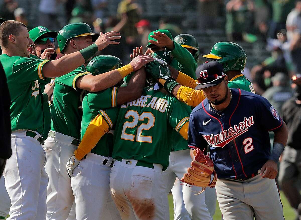 The A's mob Ramon Laureano (22) as Twins third baseman Luis Arraez (2) runs by after he reached on a throwing error by Arraez scoring two runs as the Oakland Athletics defeated the Minnesota Twins 13-12 in 10 innings at the Oakland Coliseum in Oakland, Calif., on Wednesday, April 21, 2021.