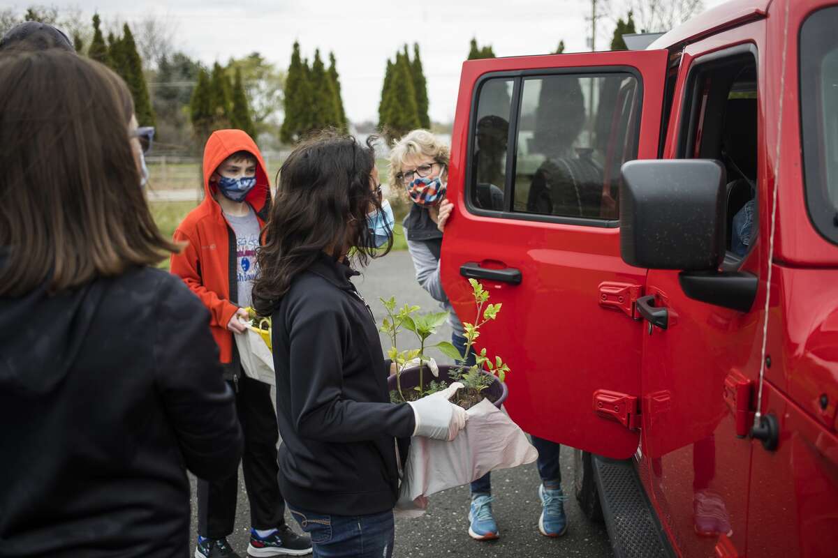 Jefferson Middle School students Sam Schroden, left, and Nellie Rueda, center, load plants into a vehicle for Billie Dush, right, as they work with classmates to pass out potted flowers and vegetables to flood victims Saturday, April 24, 2021 at the Islamic Center of Midland. (Katy Kildee/kkildee@mdn.net)