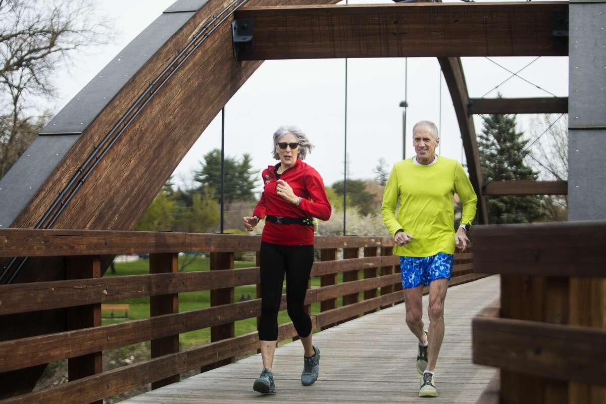 Bill Leibfritz of Midland, right, and his wife Stephanie Leibfritz, left, cross the Tridge as they go for a run together Tuesday, April 27, 2021 in Midland. Bill has gone running every day for the past 39 years. (Katy Kildee/kkildee@mdn.net)