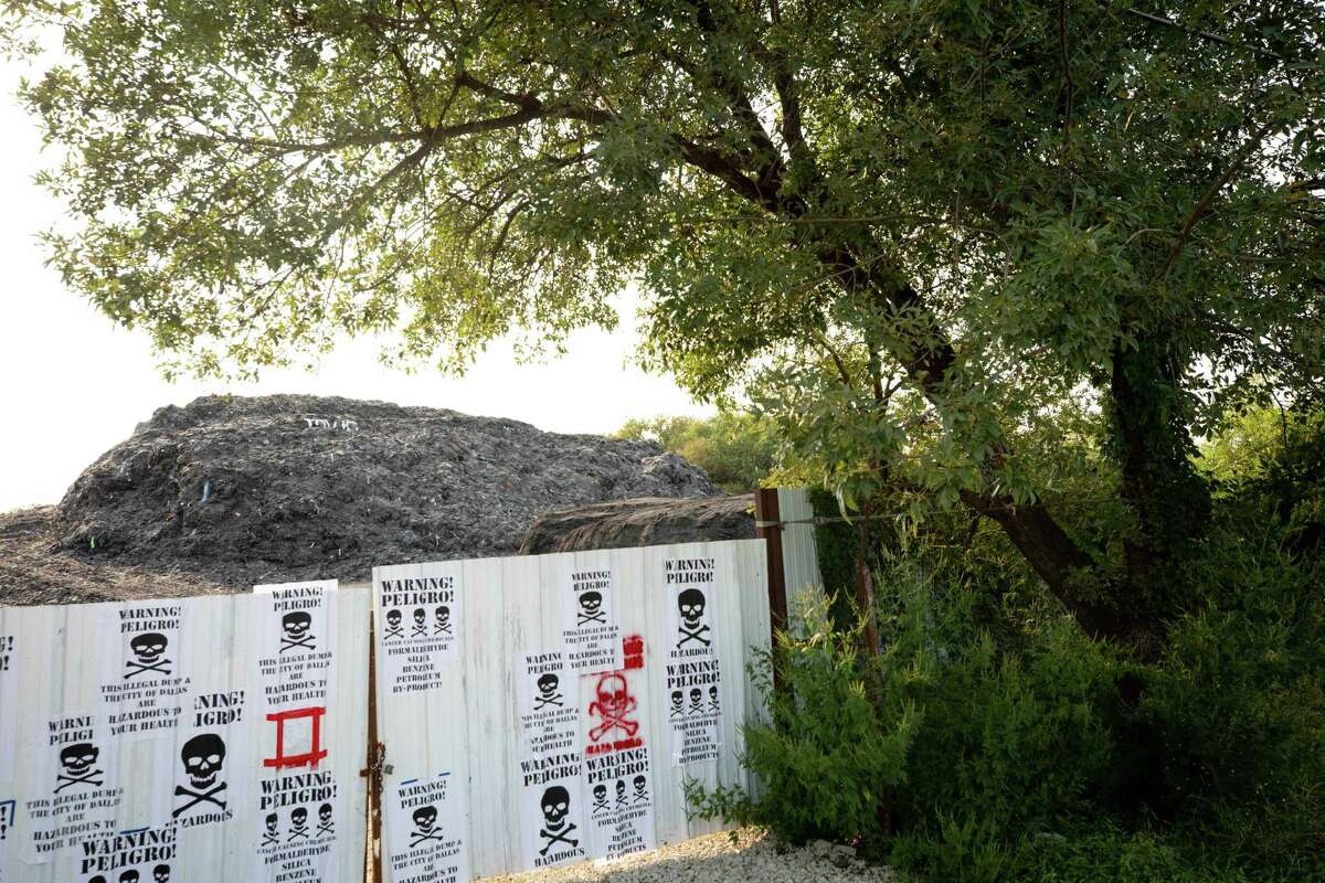 Protest signs are pasted on the gate outside a mountain of shingles at the former Blue Star Recycling property in Dallas.