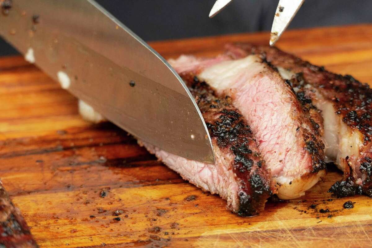 Steak is sliced on a cutting board after being reverse seared on both a smoker and a grill. The process exposes the steaks to low heat to cook them to the proper internal temperature.