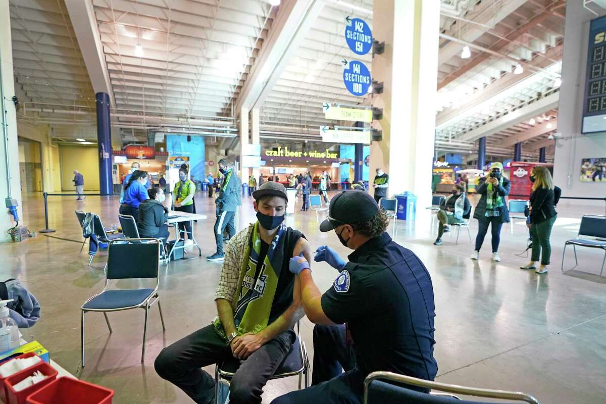 FILE - In this May 2, 2021, file photo, Austin Kennedy, left, a Seattle Sounders season ticket holder, gets the Johnson & Johnson COVID-19 vaccine at a clinic in a concourse at Lumen Field prior to an MLS soccer match between the Sounders and the Los Angeles Galaxy. Air travel in the U.S. hit its highest mark since COVID-19 took hold more than 13 months ago, while European Union officials are proposing to ease restrictions on visitors to the continent as the vaccine rollout sends new cases and deaths tumbling in more affluent countries.