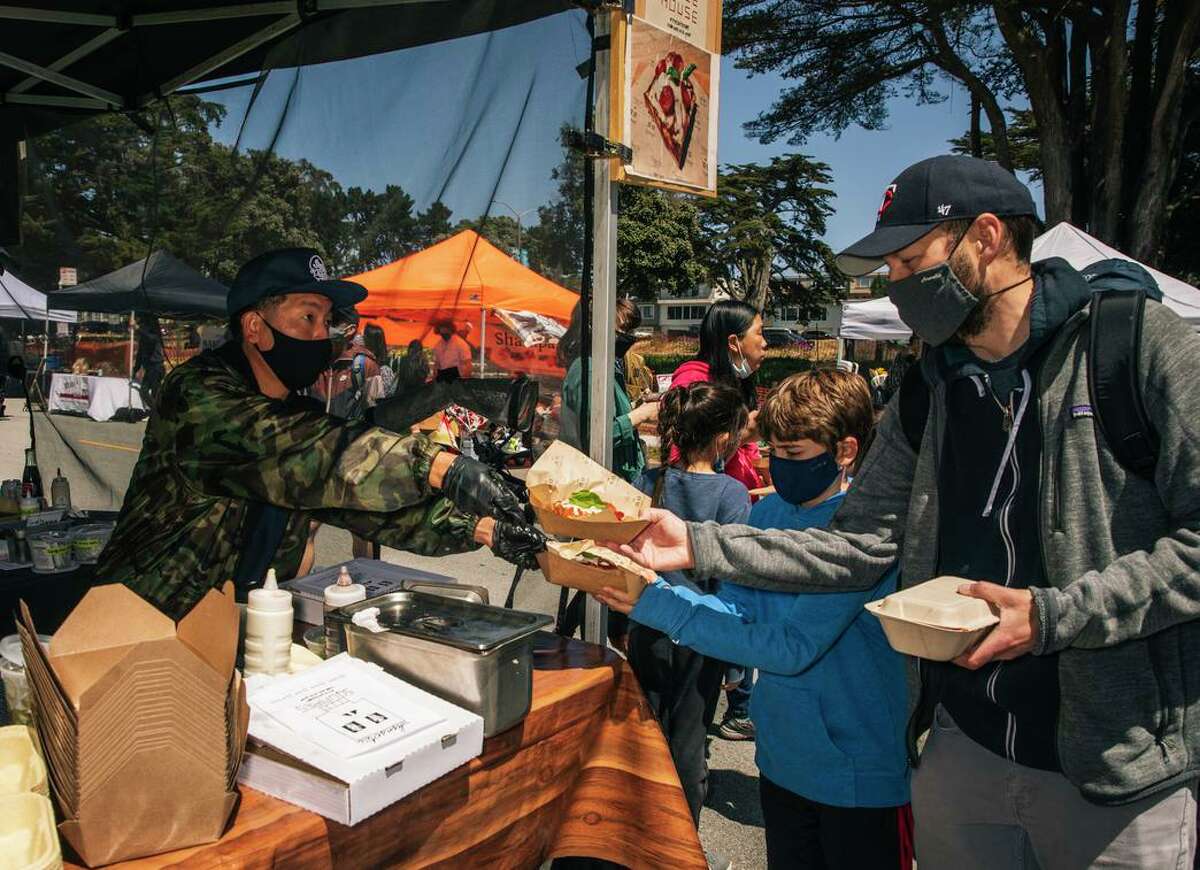 David Lee of Sunset Squares Pizza hands over an order of pizzas to customers from behind the counter at the Outer Sunset Farmer's Market & Mercantile in San Francisco, Calif. May 2, 2021.