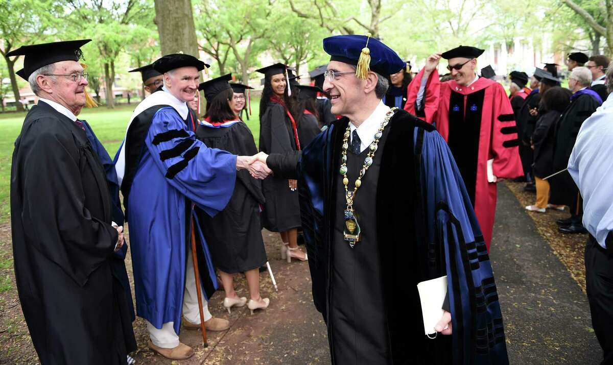 Yale University Chief Investment Officer David Swensen, left, shakes hands with Yale University President Peter Salovey, center, during Yale’s 318th Commencement as the procession makes its way through the Upper Green in New Haven on May 20, 2019.