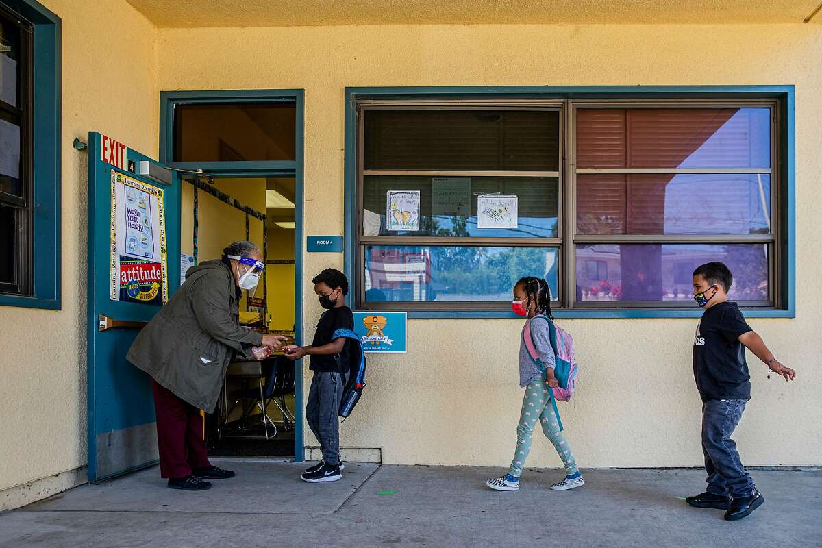 Eulalia Thomas gives Cameron Brown, 7, and other first-graders hand sanitizer as they enter class at Cleveland Elementary School in Oakland.