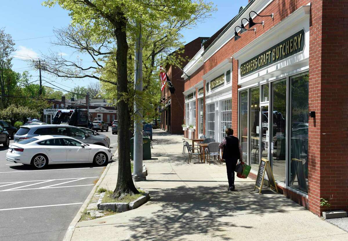 A woman walks on the sidewalk in the retail hub of downtown Cos Cob in Greenwich, Conn. Thursday, May 6, 2021.