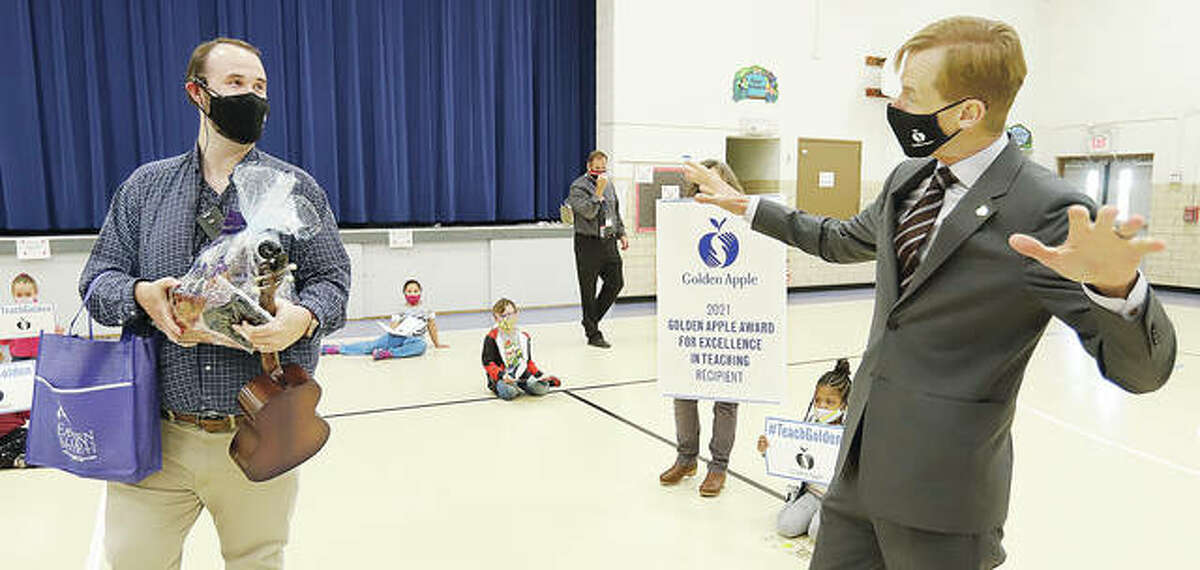 Lovejoy Elementary School music teacher Zebulon Holder, left, gets surprised Monday by Golden Apple President Alan Mather as he announces Holder as one of just 10 Illinois teachers to recieve the Golden Apple Award for Excellence in Teaching this year.