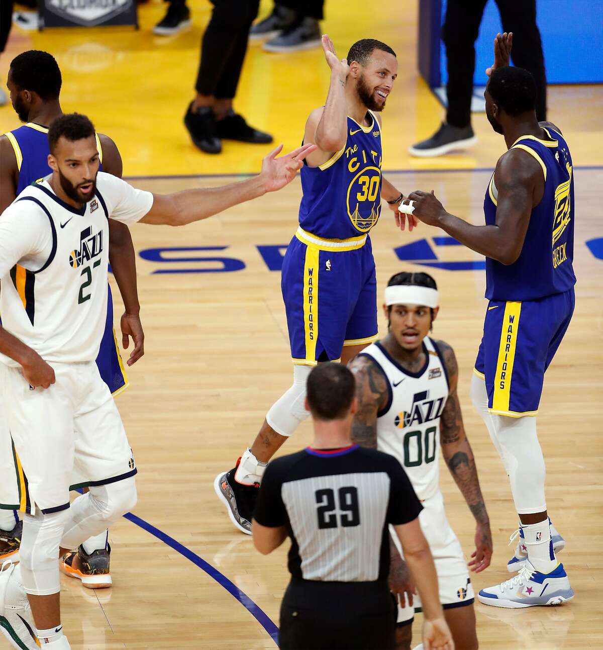 After hitting the go-ahead trey, the Warriors’ Stephen Curry high-fives Draymond Green as Jazz players question an official.