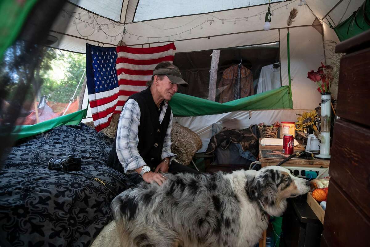 Mark Beckner plays with his dog George inside his tent at the Friendship Garden homeless encampment at Harvey West Park in Santa Cruz. The city has recently told Beckner and his neighbors that they can no longer stay there.