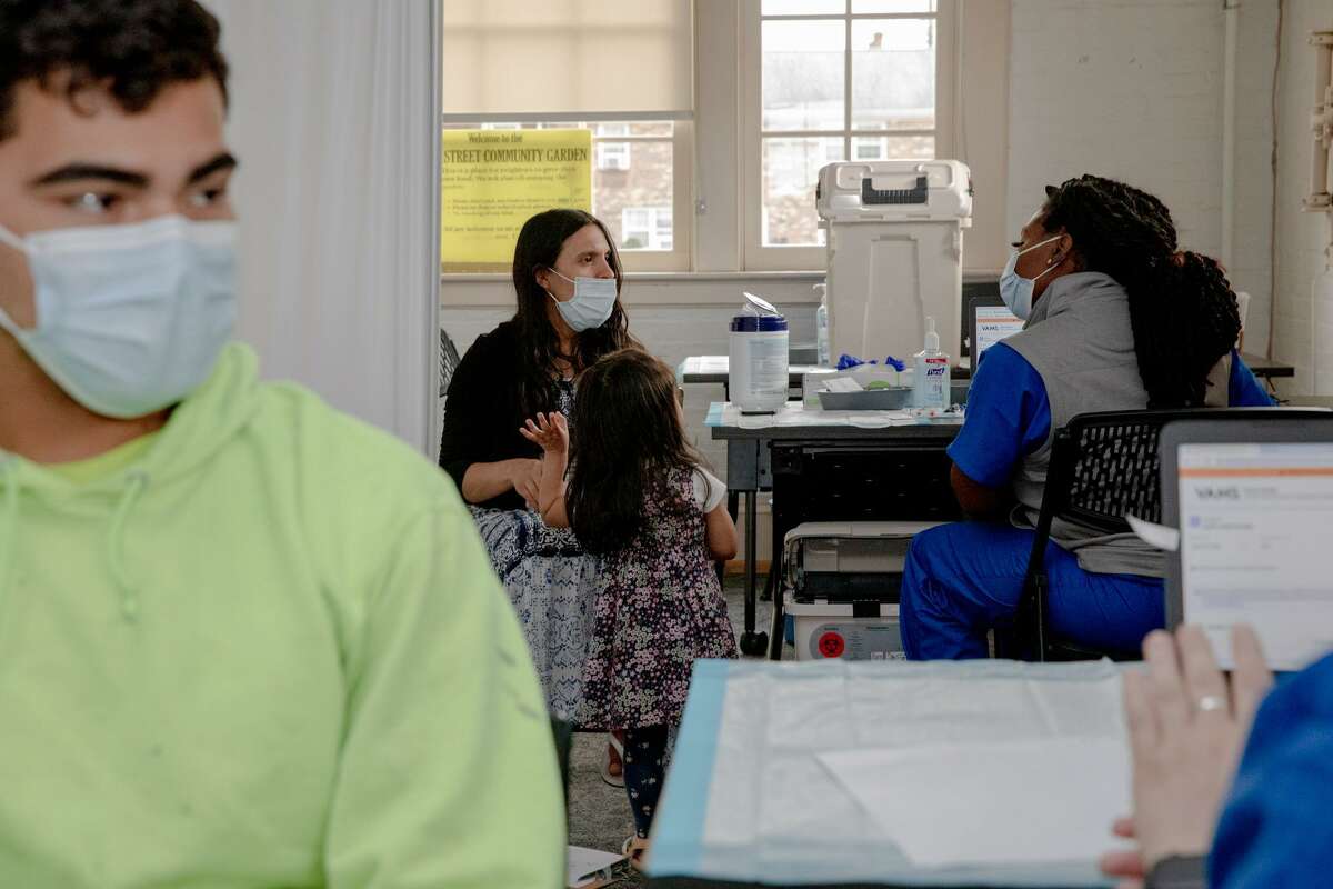Mirsa Montufar, second from left, listens to the medical personnel, Stephanie Brown, before receiving her vaccine at the Griffin mobile clinic in Manchester. Her husband, Jose Valenzuela, left, said that he didn't plan to get vaccinated at first, but his church convinced him to come to the walk-in vaccination site with his wife.