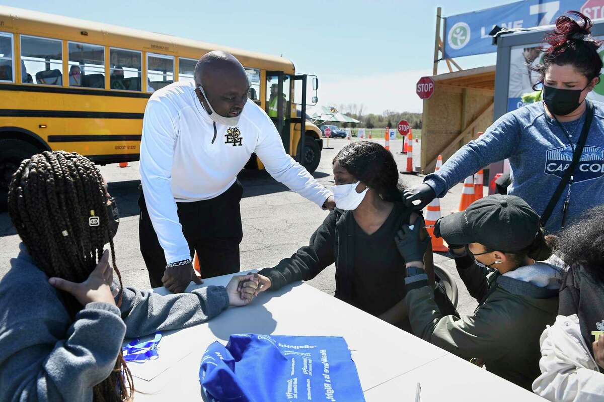 In this April 26, 2021, file photo, East Hartford High School senior Sudeen Pryce, right, center, receives support from classmate Alexia Phipps, left, East Hartford High School Intervention Coordinator Mark Brown, second from left, and EMT Katrinna Greene, top right, of Manchester, as RN Kaylee Cruz of Bristol administers the first dose of the Pfizer vaccine to Pryce at a mass vaccination site at Pratt & Whitney Runway in East Hartford.