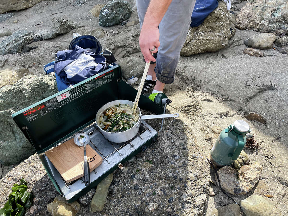 Spencer Marley cooks seaweed ramen on the beach.