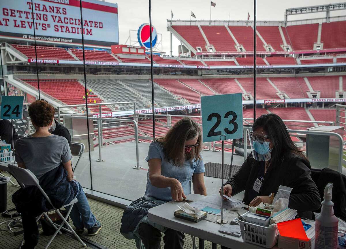 Lynda Barbieri, center, checks in with clinical nurse Lynette Ancheta, right, before recieving her Pfizer COVID-19 vaccine at Levi’s Stadium in Santa Clara on Feb. 9, 2021. Santa Clara County advanced Tuesday into the yellow tier, the least restrictive level of California’s color-coded pandemic reopening system.