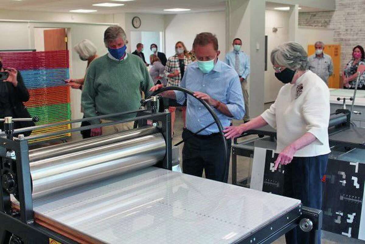 Gov. Ned Lamont, center, tries out the new printing press at Five Points Center for the Arts during his May 14 visit. He is pictured with the center's board president, Eric Forstmann, left, and executive director Judy McElhone.