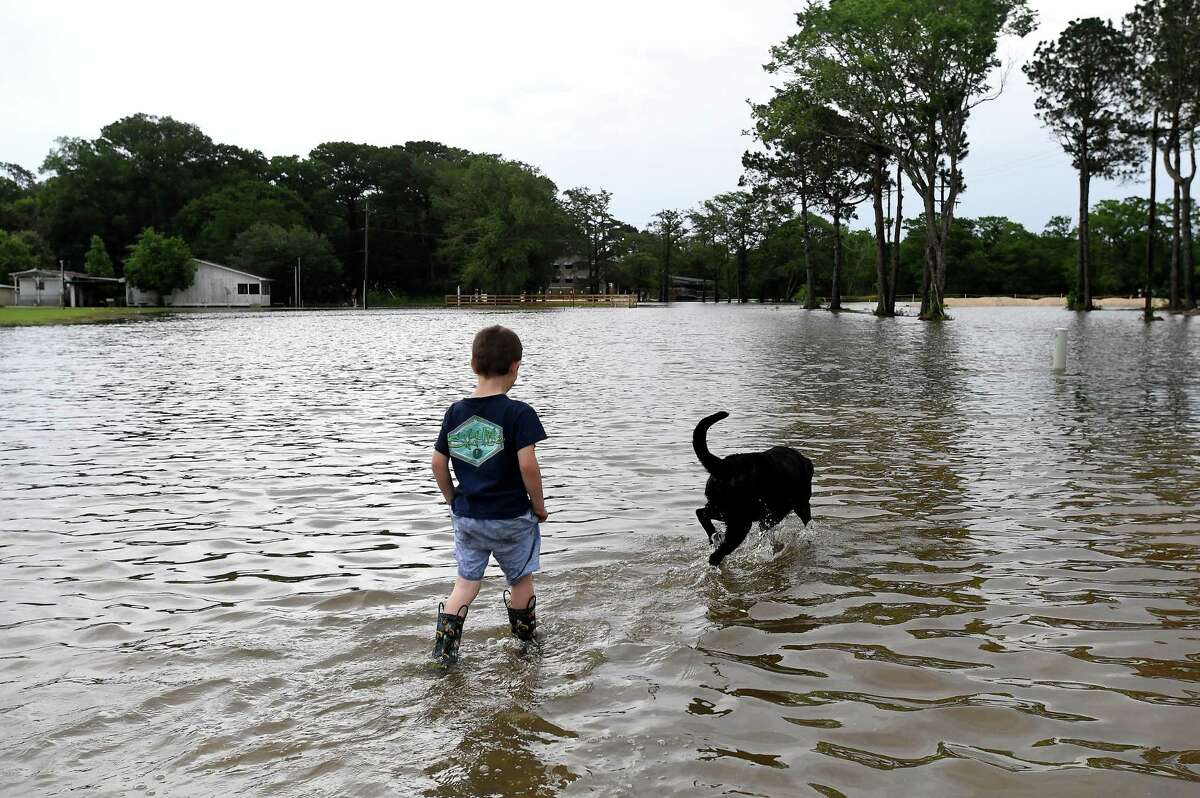 Jason Johnson and a neighborhood dog play in spillover flooding from Taylor's Bayou along LaBelle Road near Pine Tree Lodge as he and his grandfather Thomas Robin assess the conditions in Fannett Tuesday. The area received over a foot of rainfall Monday, flooding area bayous and several yards and homes. Photo made Tuesday, May 18, 2021 Kim Brent/The Enterprise