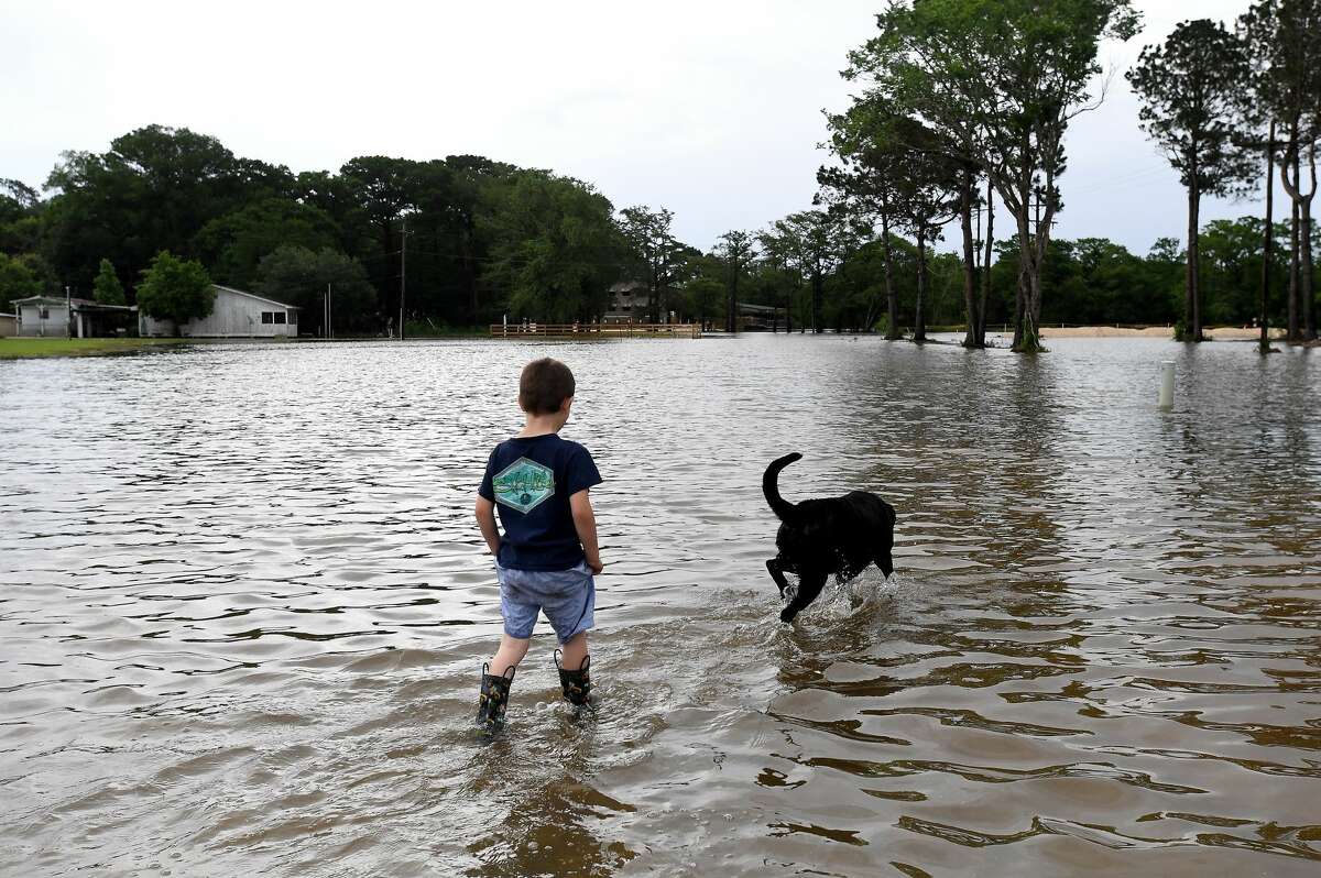 Jason Johnson and a neighborhood dog play in spillover flooding from Taylor's Bayou along LaBelle Road near Pine Tree Lodge as he and his grandfather Thomas Robin assess the conditions in Fannett Tuesday. The area received over a foot of rainfall Monday, flooding area bayous and several yards and homes. Photo made Tuesday, May 18, 2021 Kim Brent/The Enterprise