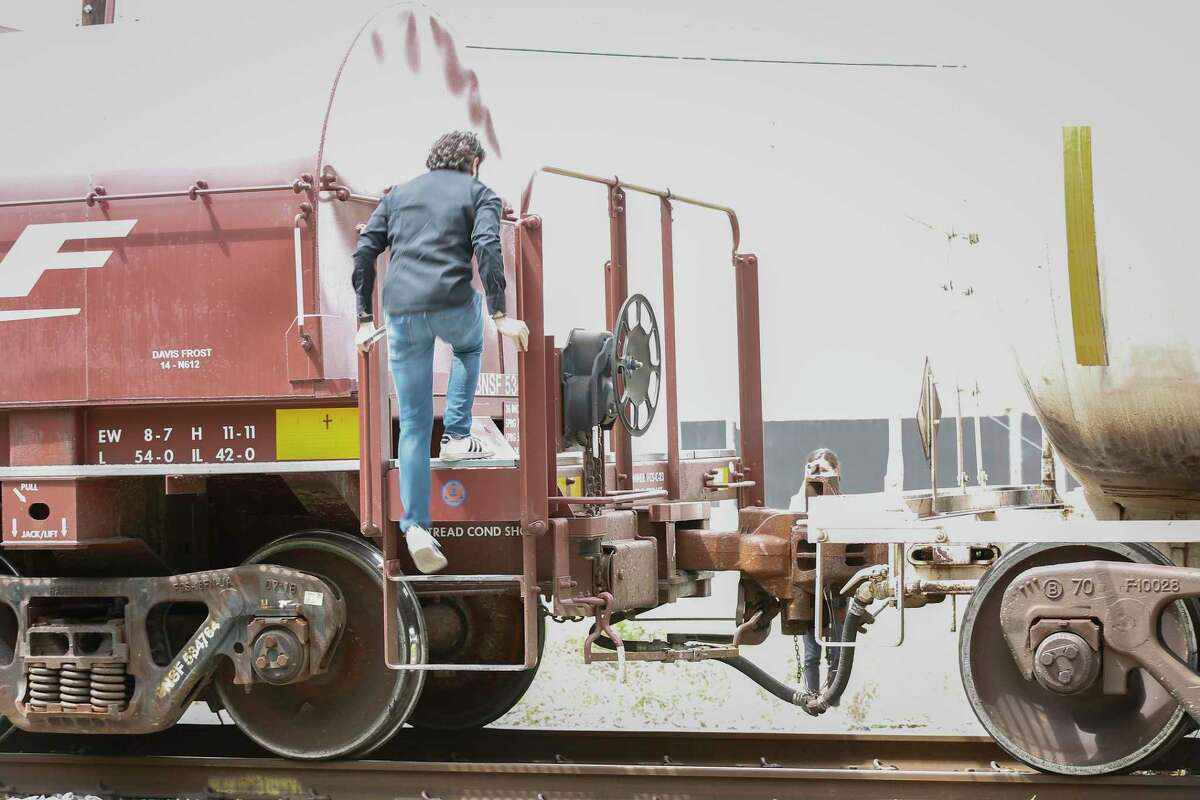 Pedestrians climb over railroad cars after a train stopped for more than 45 minutes on the tracks across Lockwood Avenue on May 18, 2021, in Houston.