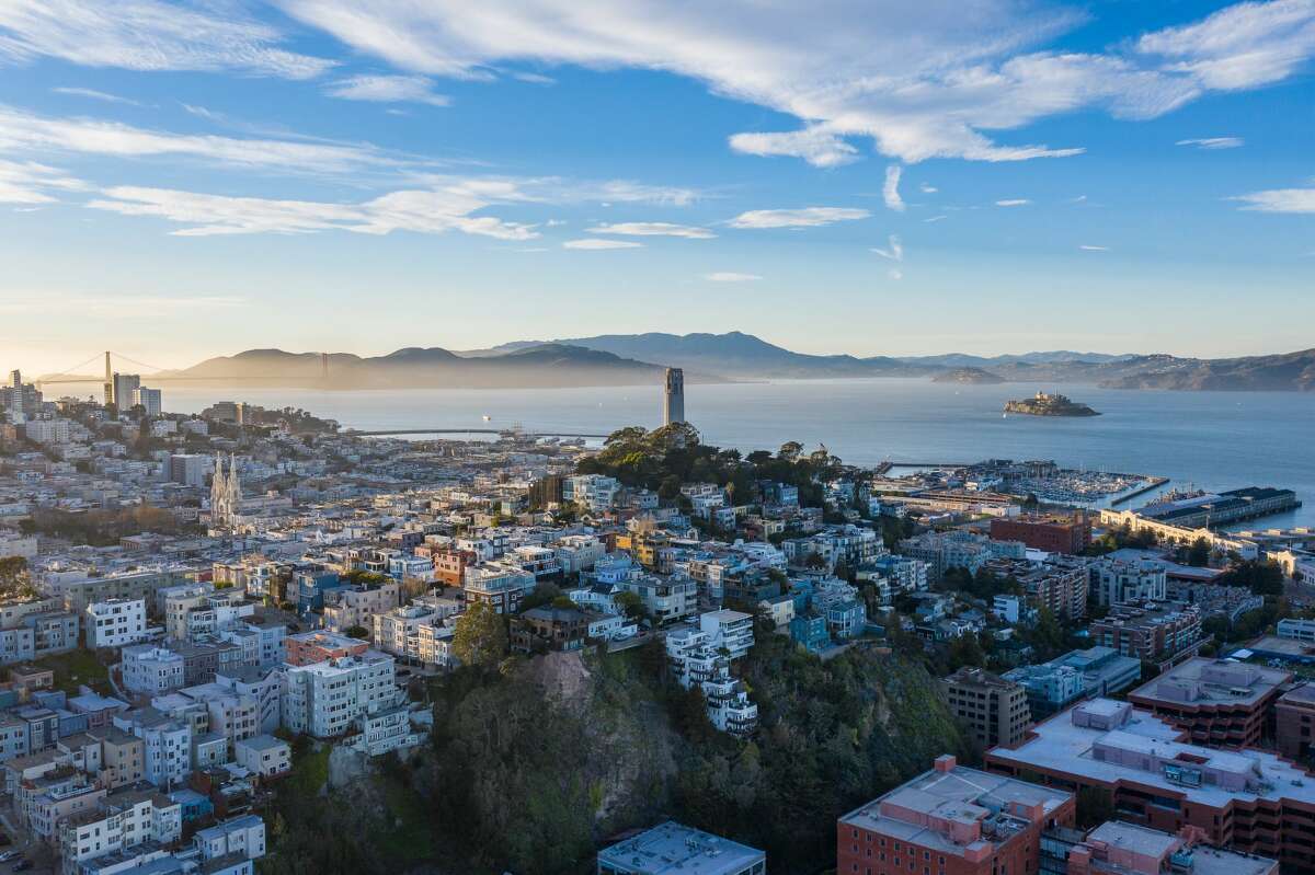 Aerial view of Coit Tower and Russian Hill as the sun begins to set. Alcatraz is visible in the bay and the Golden Gate bridge in the distance.