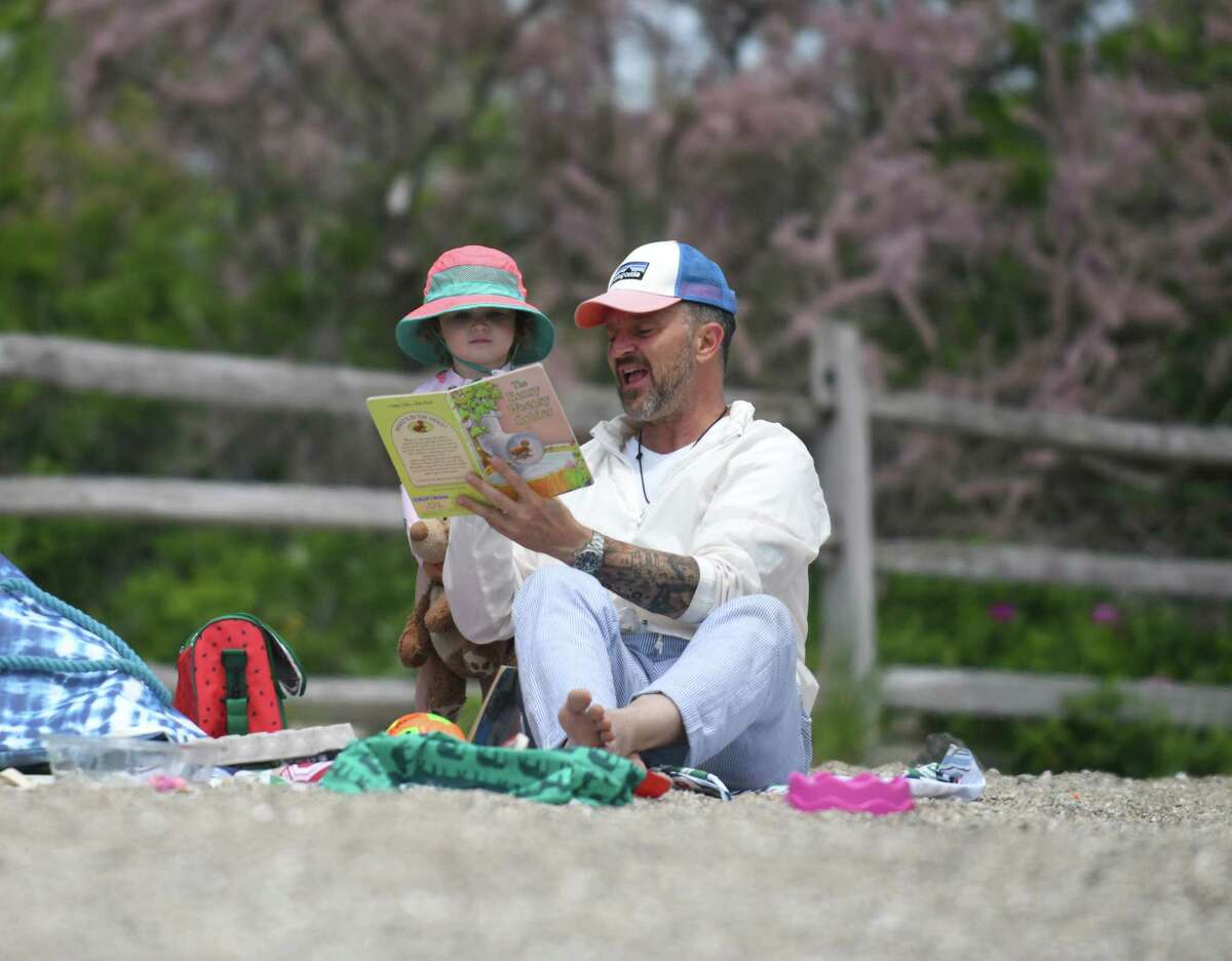 Geoffrey Nichols, visiting from St. Petersburg, Fla., reads a book to his neice Charlotte Gray, 2, on the beach at Greenwich Point Park in Old Greenwich, Conn. Thursday, May 20, 2021.